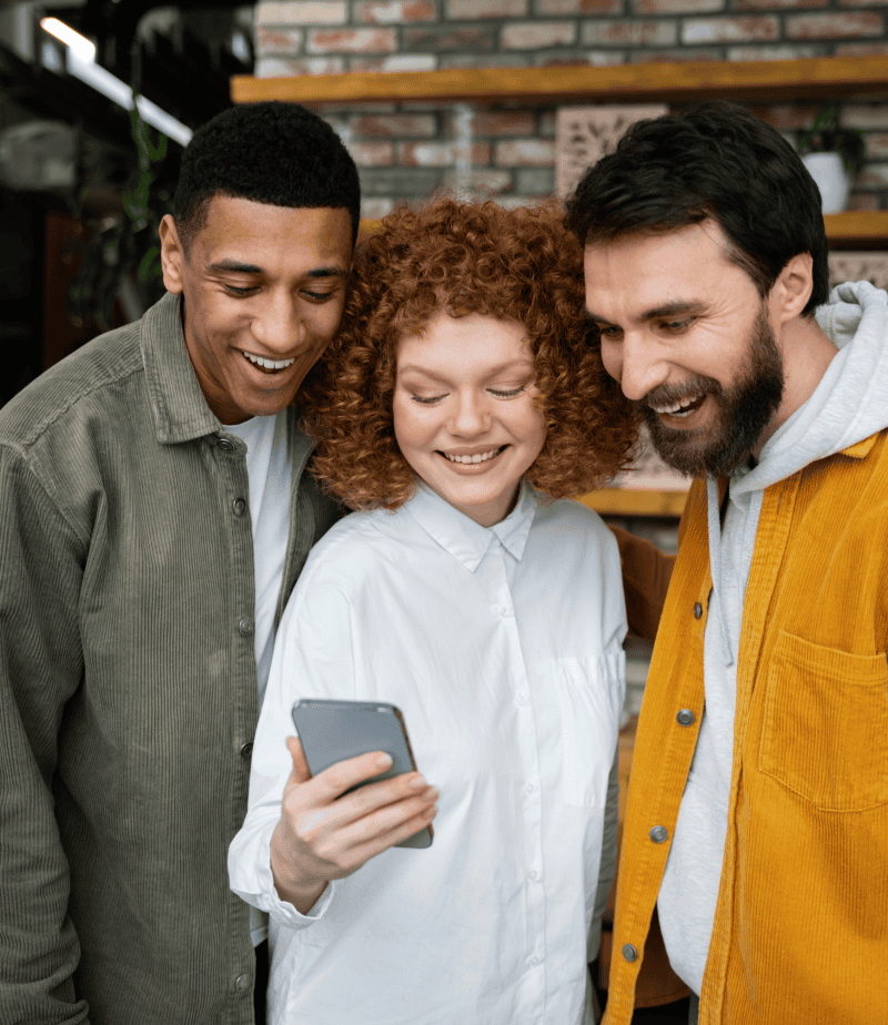 Brightly smiling group of diverse young adults looking at a smartphone, representing digital experience, social media, and technology engagement.