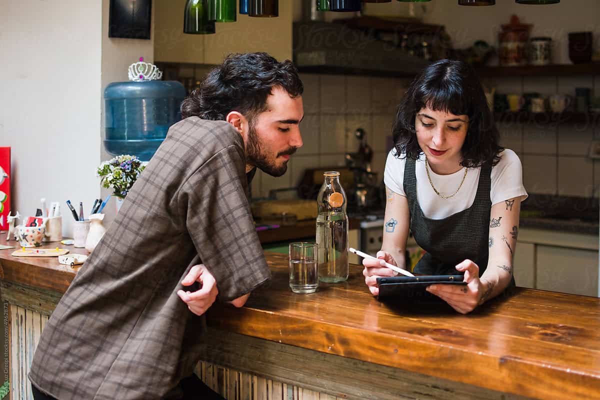 Young woman and man discussing business digital marketing at cafe bar, using tablet, working together, casual office environment, teamwork, digital collaboration, modern workspace, creative entrepreneurs, digital marketing services.